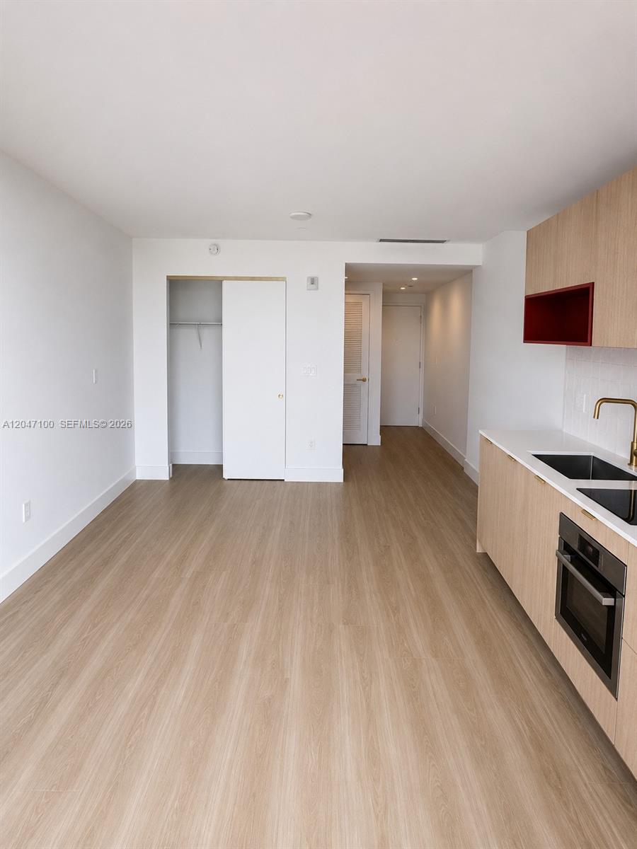 An interior view shows a kitchen with light wood cabinets and a white-walled living area — 90 NE 32nd St # 1126, Miami FL 33127, MIAMI, FL