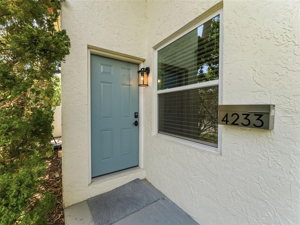 A blue front door sits next to a window and a house number sign — 4233 LA SORRENTO COURT, TAMPA, FL