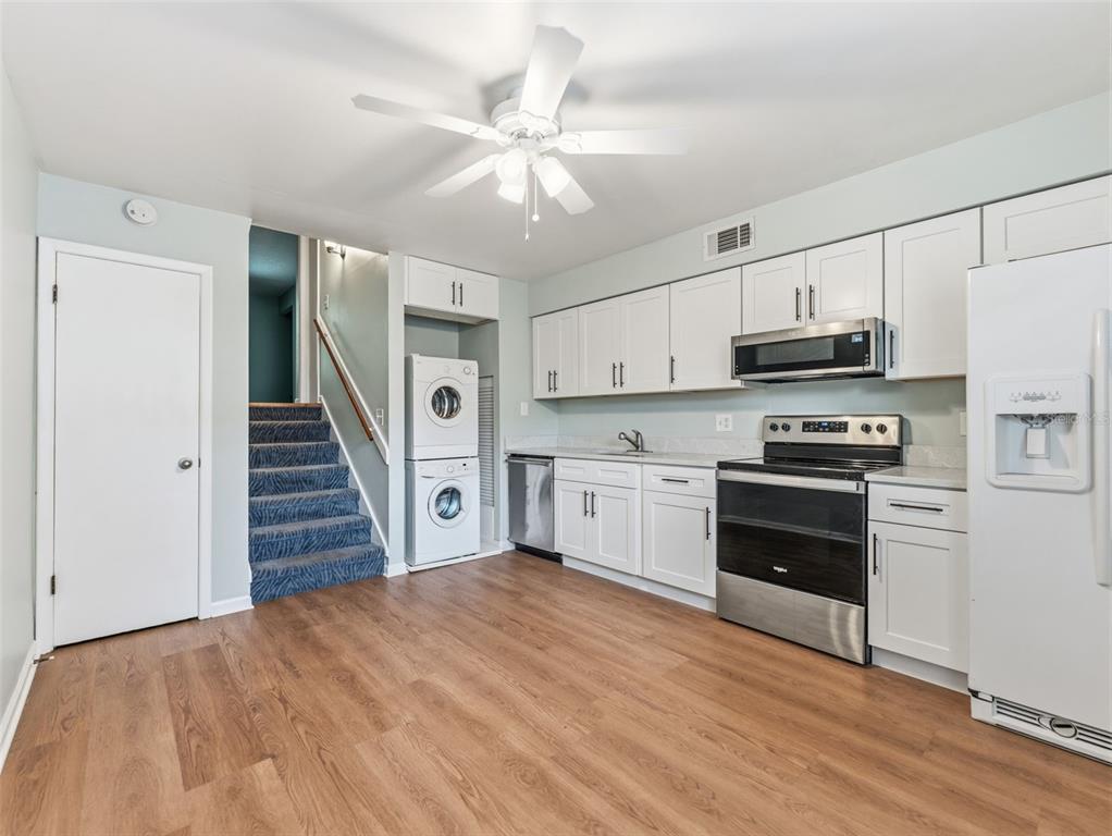 A kitchen with white cabinets, stainless steel appliances, wood-look flooring, and a stacked laundry unit — 4233 LA SORRENTO COURT, TAMPA, FL