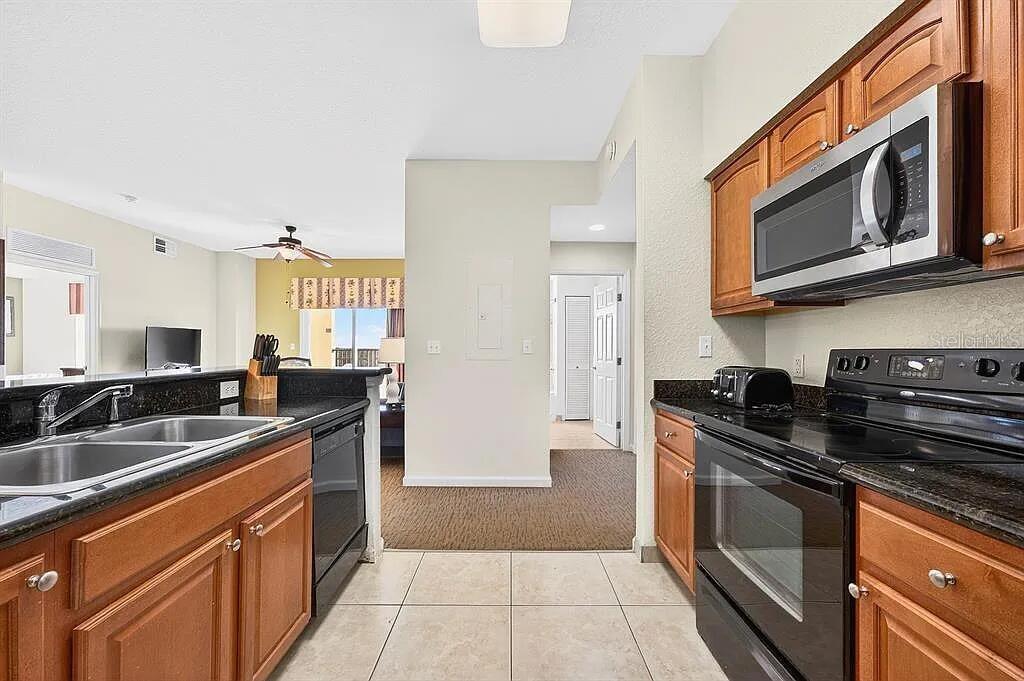 A kitchen features wood cabinets, black appliances, and granite countertops with a view of the living area — 8101 RESORT VILLAGE DRIVE UNIT 3401, ORLANDO, FL