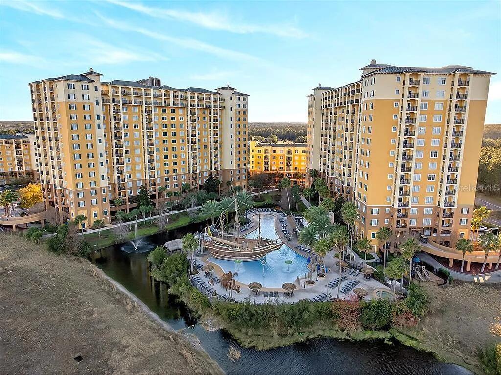 An aerial view shows two tall yellow apartment buildings surrounding a pool with a ship structure — 8101 RESORT VILLAGE DRIVE UNIT 3401, ORLANDO, FL