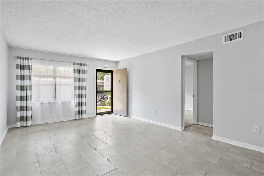 A bright living room features light gray tile flooring, white walls, and a glass-paneled front door — 4920 LOCUST STREET NE UNIT 115, ST PETERSBURG, FL