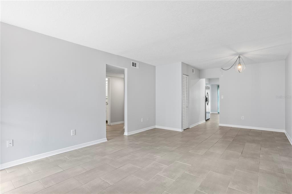 A bright, open-concept living area features light gray walls, neutral tile flooring, and a chandelier — 4920 LOCUST STREET NE UNIT 115, ST PETERSBURG, FL