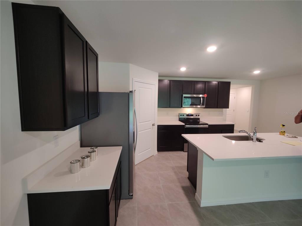 A kitchen features dark cabinets, white countertops, a stainless steel refrigerator, and a center island — 11284 SE 67TH CIRCLE, BELLEVIEW, FL