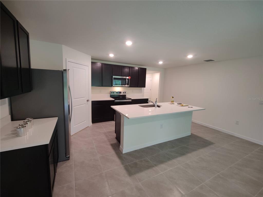 A kitchen features dark cabinets, white countertops, a central island, and light-colored tile flooring — 11284 SE 67TH CIRCLE, BELLEVIEW, FL