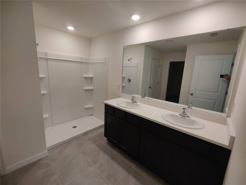 A bathroom features a double vanity with a white countertop and a walk-in shower — 11284 SE 67TH CIRCLE, BELLEVIEW, FL
