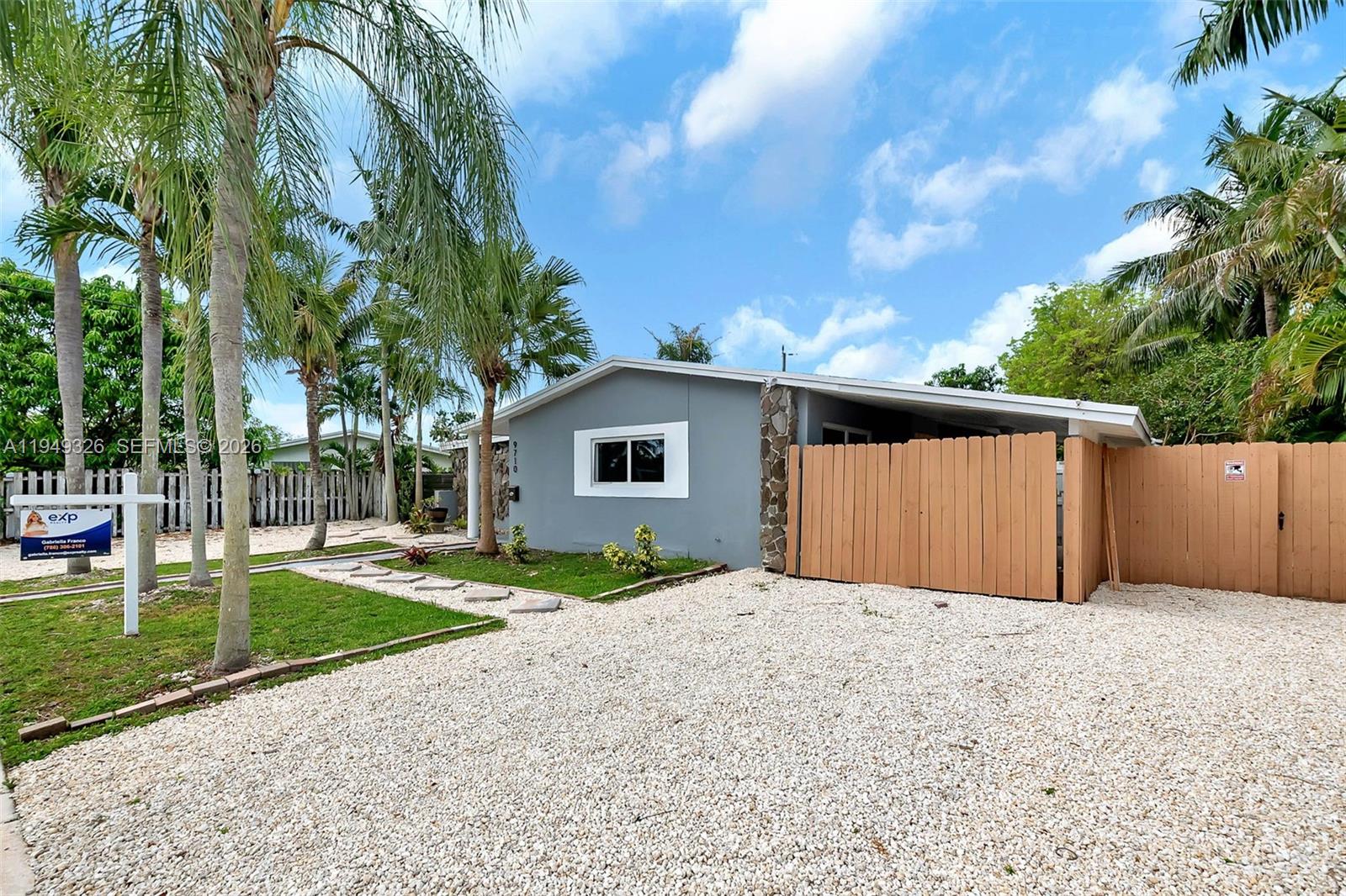 A gray single-story house features a stone accent wall, a gravel driveway, and wooden fencing — 9710 SW SW 161 ST, Miami FL 33157, MIAMI, FL