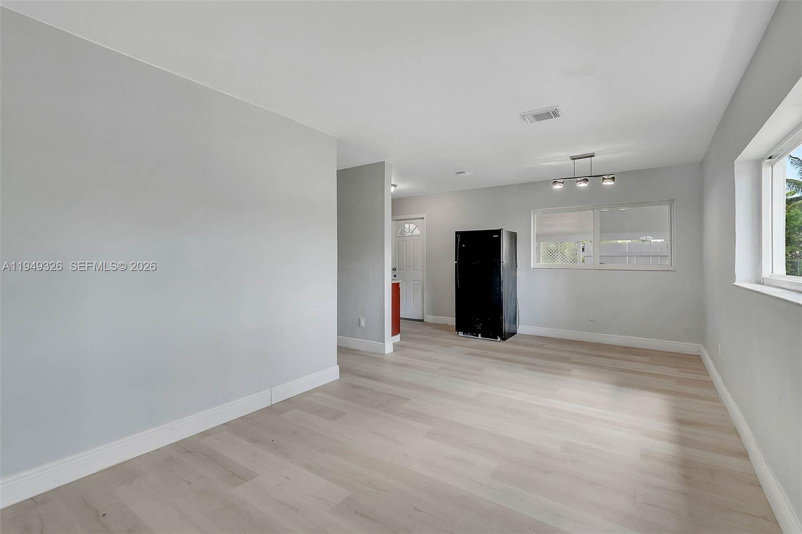An empty room features light wood-look flooring, gray walls, a black refrigerator, and a window — 9710 SW SW 161 ST, Miami FL 33157, MIAMI, FL