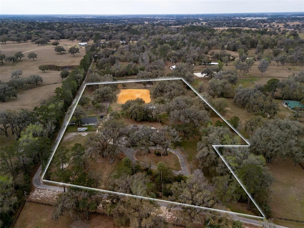 An aerial view shows a house and a sandy riding arena on a wooded lot — 4986 SW 7TH AVENUE ROAD, OCALA, FL