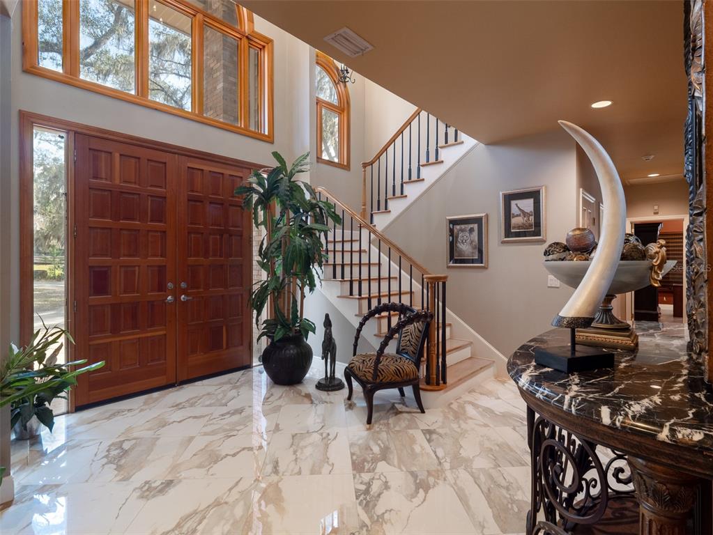 A grand foyer features marble flooring, a wooden double door, and a staircase with railings — 4986 SW 7TH AVENUE ROAD, OCALA, FL