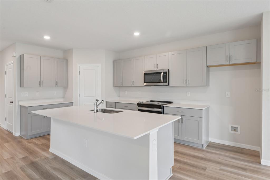 A modern kitchen features gray cabinets, white countertops, a central island, and wood-look flooring — 4192 RIVER BEACON BOULEVARD, DAVENPORT, FL
