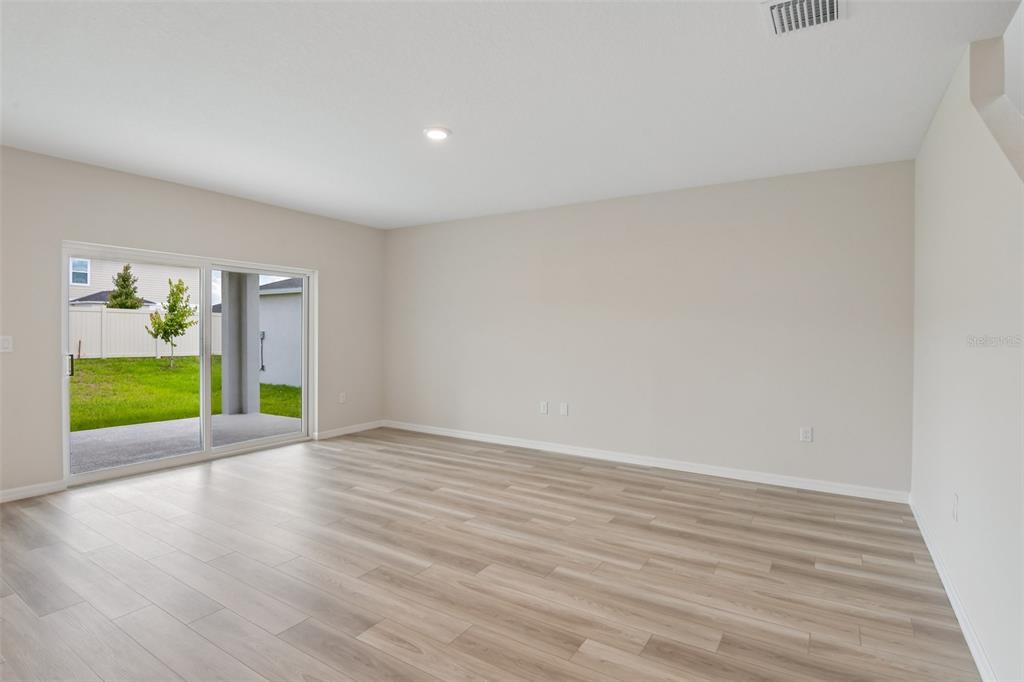 An empty room with light wood-look flooring, beige walls, and a sliding glass door — 4192 RIVER BEACON BOULEVARD, DAVENPORT, FL