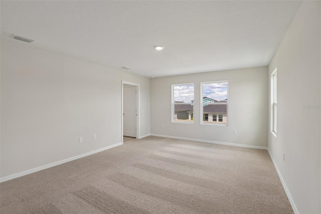 An empty bedroom features beige carpet, light-colored walls, and two windows overlooking a neighborhood — 4192 RIVER BEACON BOULEVARD, DAVENPORT, FL