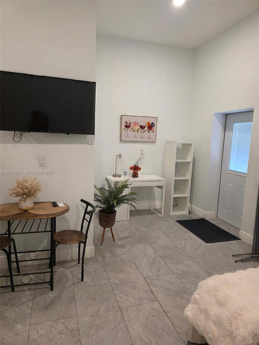 This room features light gray tile flooring, a wall-mounted television, a small dining set, and a desk — HOMESTEAD, FL