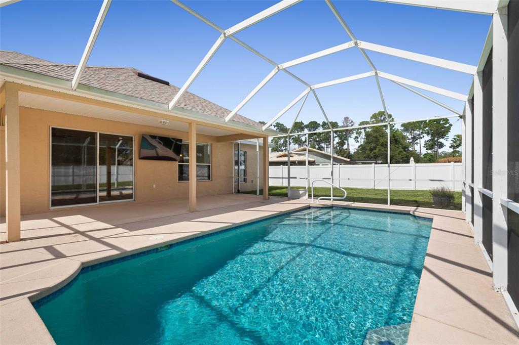 A swimming pool sits inside a screened-in lanai attached to the back of a house — 62 FORRESTER PLACE, PALM COAST, FL