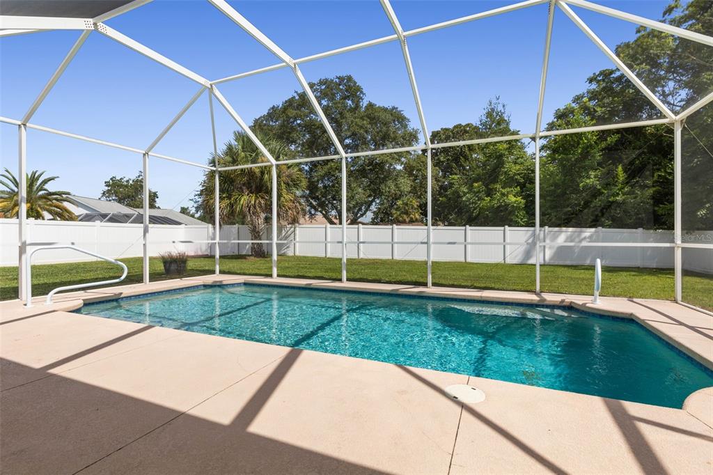 A rectangular swimming pool is enclosed by a white screen cage in a grassy backyard — 62 FORRESTER PLACE, PALM COAST, FL