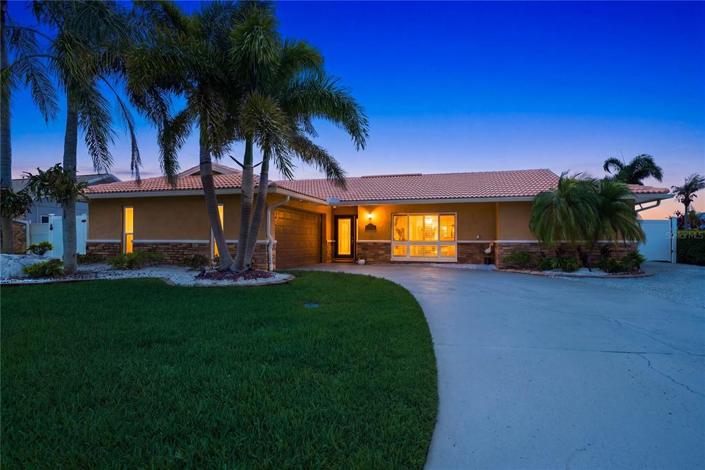 A single-story house with a tiled roof, palm trees, and a concrete driveway at dusk — 5351 PILOTS PLACE, NEW PORT RICHEY, FL