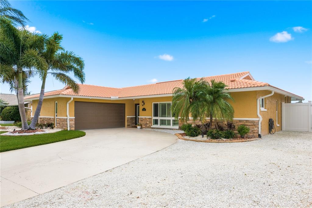 A single-story house with yellow stucco walls, a tile roof, and a gravel driveway — 5351 PILOTS PLACE, NEW PORT RICHEY, FL