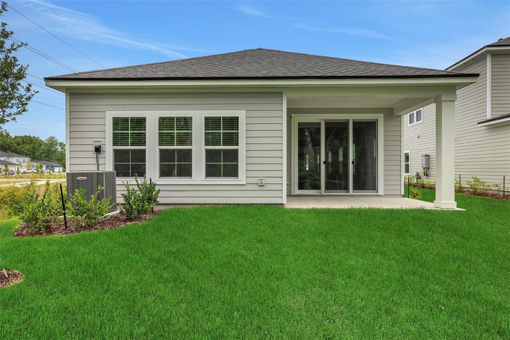 The back exterior of a light gray house features a covered patio and sliding glass doors — 530 FARMFIELD DRIVE, ST AUGUSTINE, FL