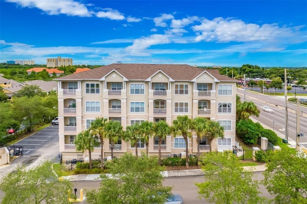 A four-story apartment building with balconies and palm trees sits next to a parking lot — 1216 S MISSOURI AVENUE UNIT 317, CLEARWATER, FL