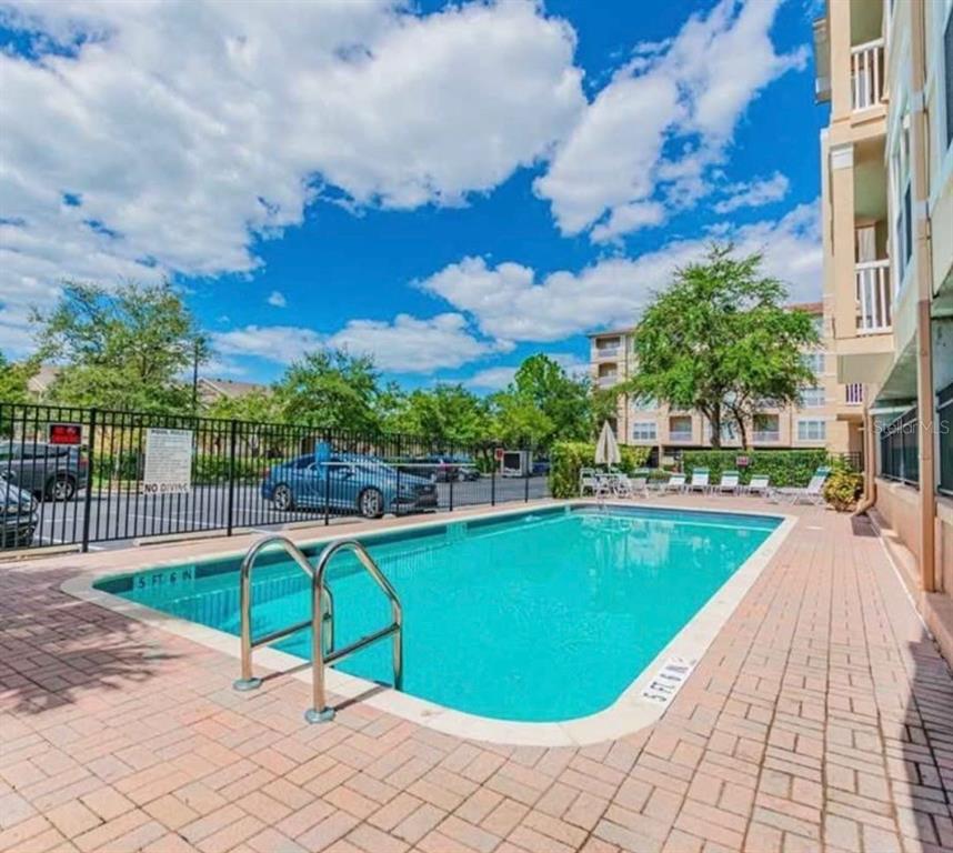 A rectangular outdoor swimming pool is surrounded by a brick patio and a black fence — 1216 S MISSOURI AVENUE UNIT 317, CLEARWATER, FL