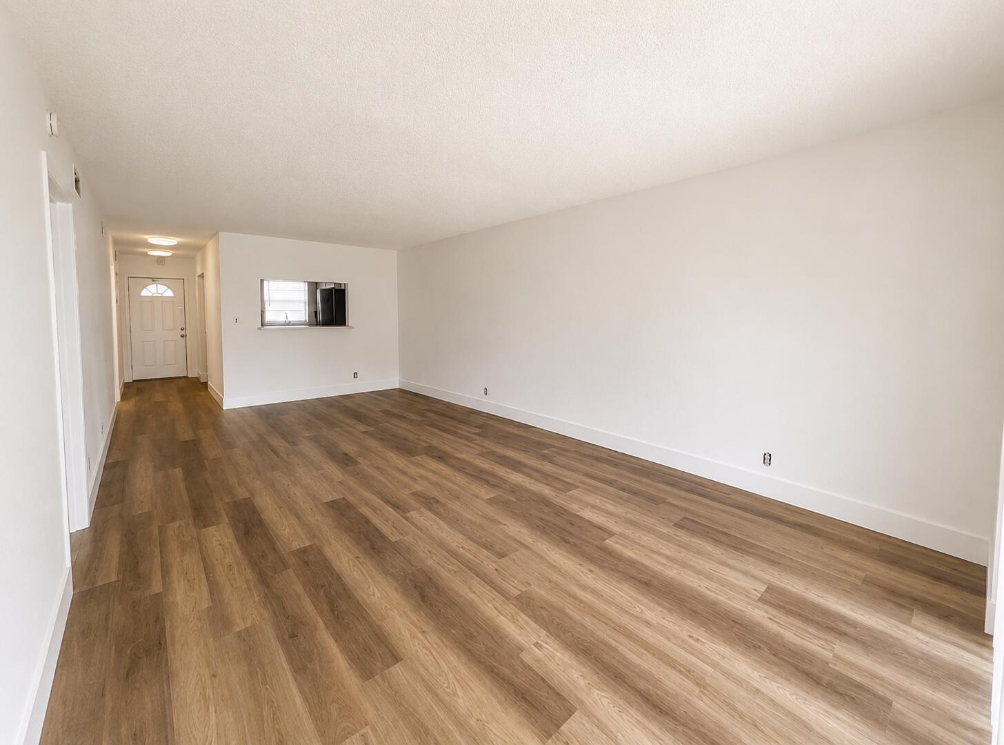 An empty living room features white walls, wood-look flooring, and a pass-through window to the kitchen — 601 S State Road 7 # 2h, Margate FL 33068, MARGATE, FL