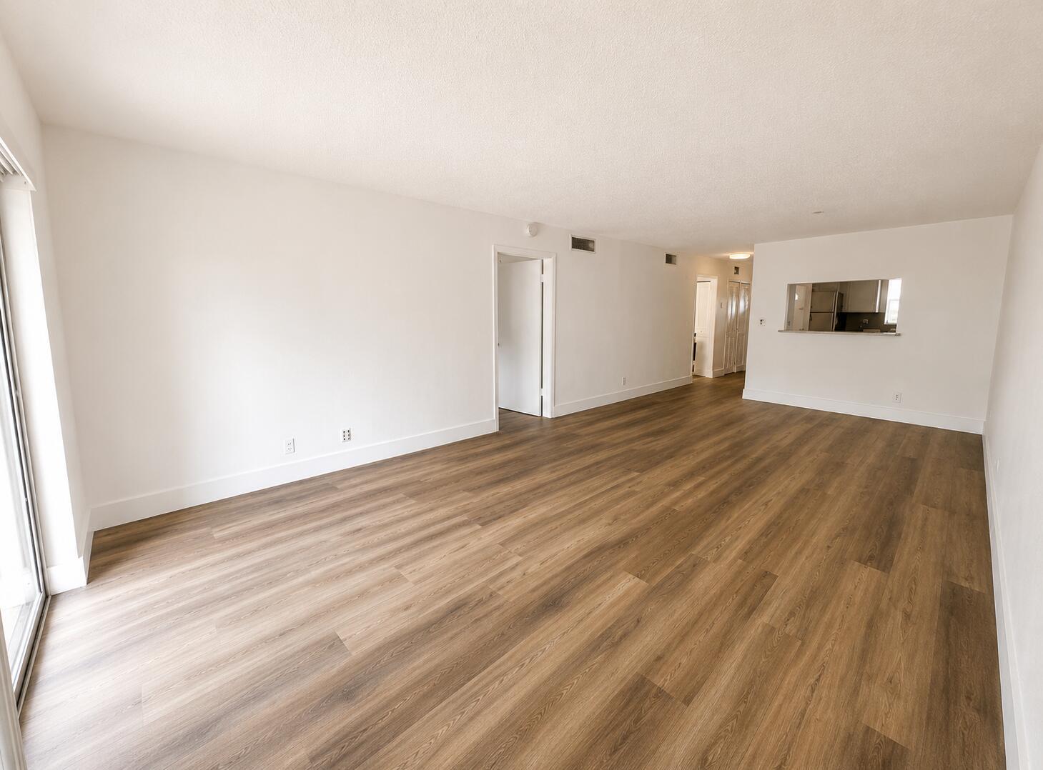 An empty living room with white walls, wood-look flooring, and a kitchen pass-through window — 601 S State Road 7 # 2h, Margate FL 33068, MARGATE, FL