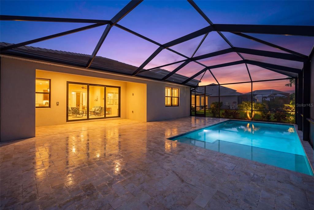A covered patio with a swimming pool and tile flooring at sunset — 12938 PINNACLE LANE, VENICE, FL