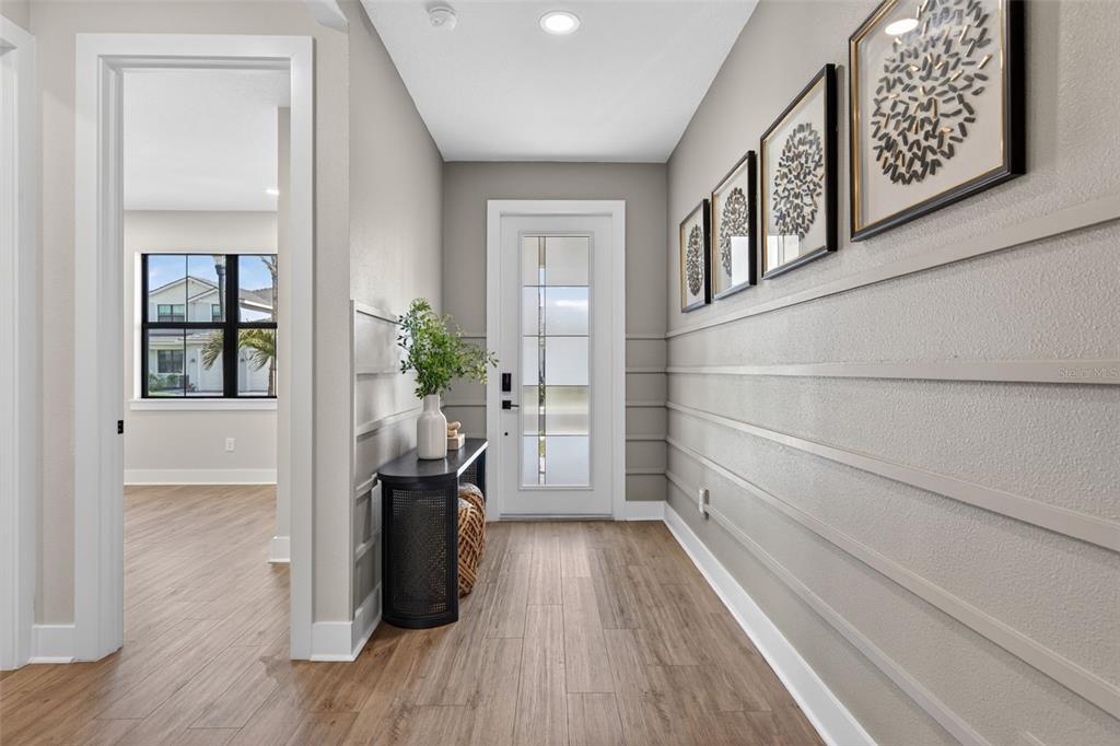A bright entryway features horizontal wall paneling, wood-look flooring, and a glass-paneled front door — 12938 PINNACLE LANE, VENICE, FL