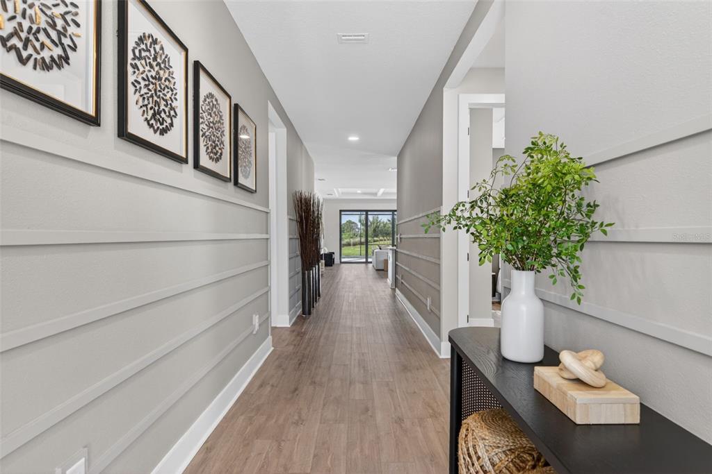 A hallway with wood-look flooring, horizontal wall trim, and a console table with decor — 12938 PINNACLE LANE, VENICE, FL