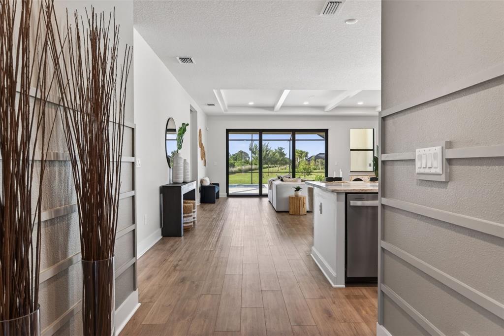 A view from a hallway into an open-concept living area with wood-look tile flooring — 12938 PINNACLE LANE, VENICE, FL