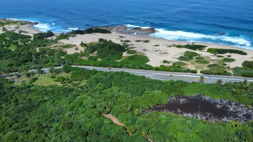 An aerial view shows a coastal landscape with a road, sandy beach, and ocean waves — SR.466 KM 11.7 BAJURA WD, ISABELA, PR