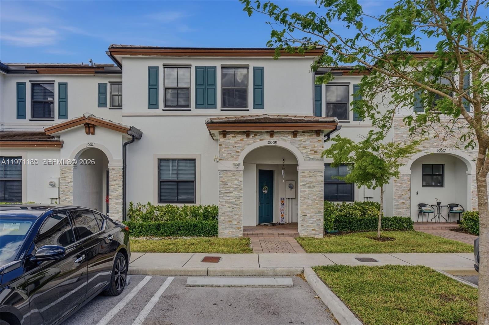 A multi-story townhouse exterior features a stone-accented entryway, teal shutters, and a paved walkway — 10009 SW 228th Ter, Miami FL 33190, MIAMI, FL