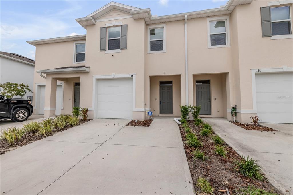 A row of three beige two-story townhouses with concrete driveways and attached garages — 148 REENA DRIVE, DAYTONA BEACH, FL