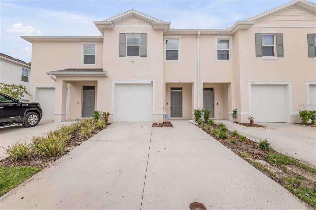 A row of two-story townhouses with beige stucco exteriors, white garage doors, and concrete driveways — 148 REENA DRIVE, DAYTONA BEACH, FL