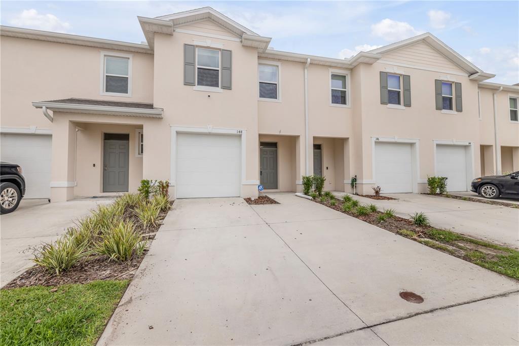 A row of light-colored townhouses with attached garages and concrete driveways under a cloudy sky — 148 REENA DRIVE, DAYTONA BEACH, FL