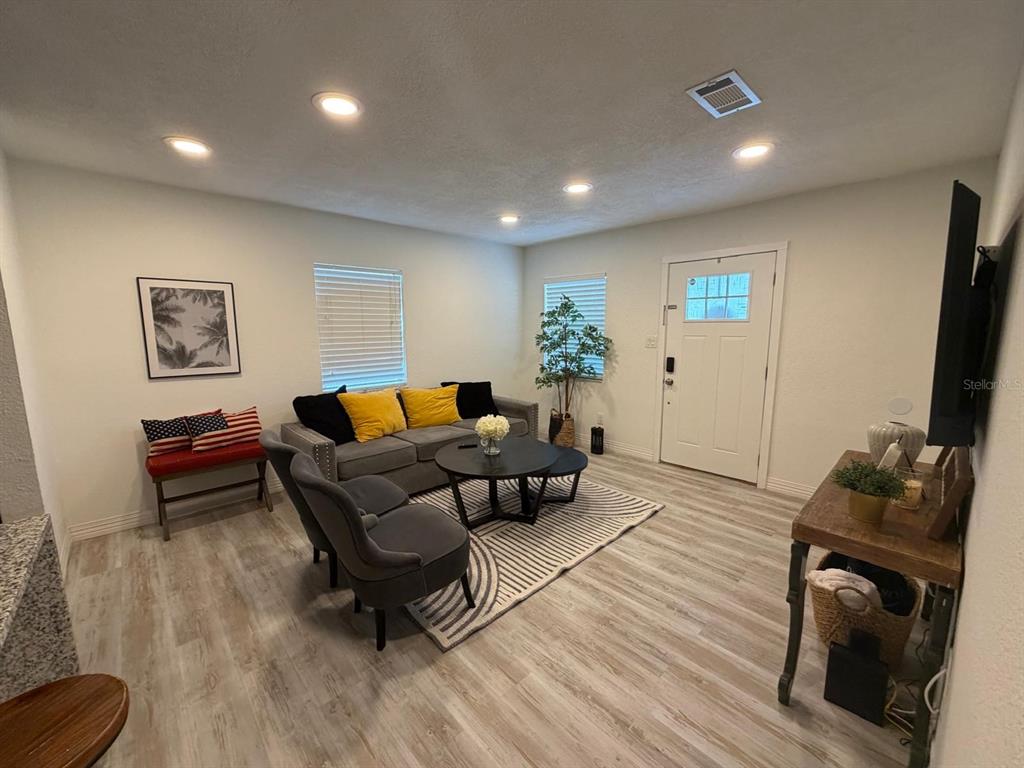 A living room features light wood-look flooring, recessed lighting, a gray sofa, and a front door — 4714 W LAWN AVENUE, TAMPA, FL
