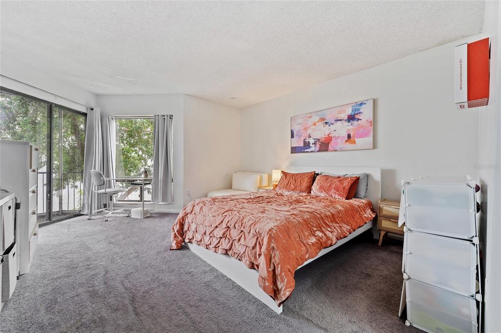 A bedroom with gray carpet, a bed with an orange comforter, and a sliding glass door — 4312 LAKEWAY DRIVE UNIT 12F, ORLANDO, FL