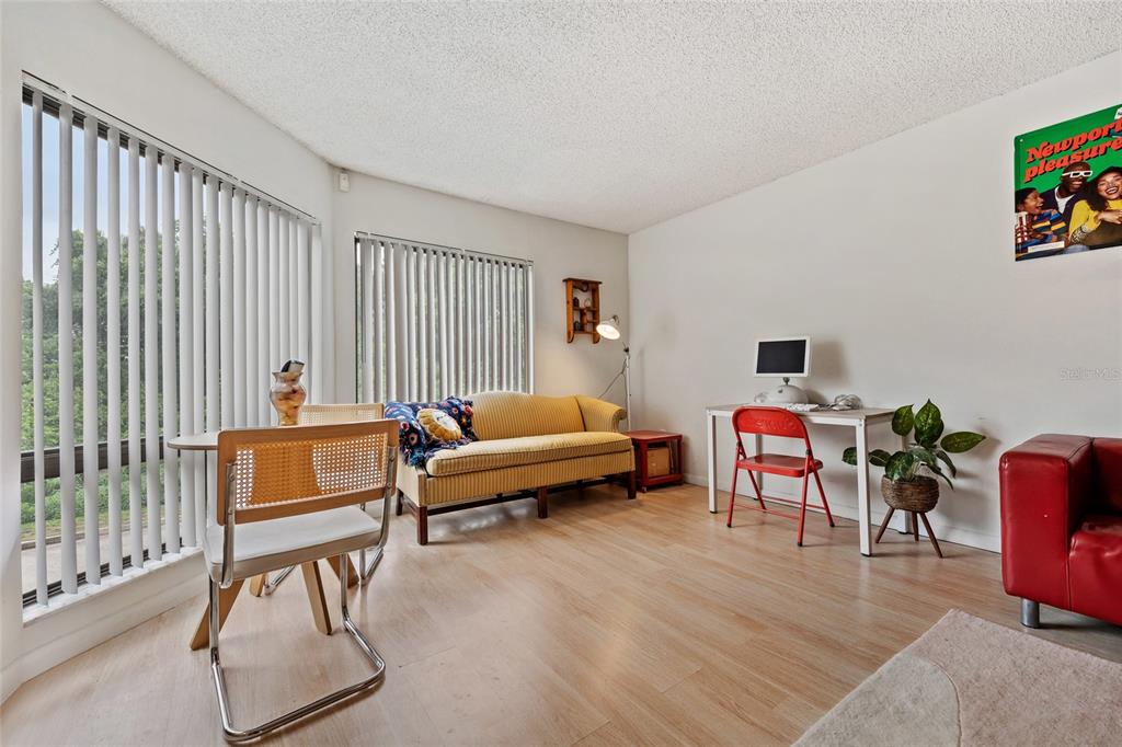 A living room features light wood-look flooring, a yellow sofa, and a desk with a chair — 4312 LAKEWAY DRIVE UNIT 12F, ORLANDO, FL