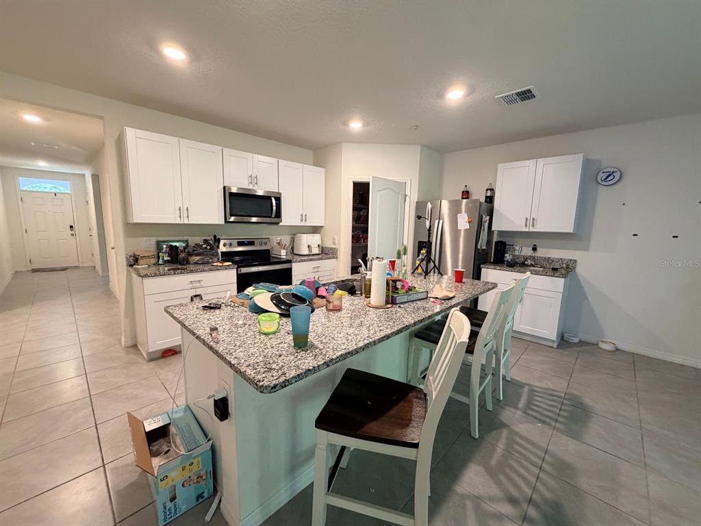 A kitchen features white cabinets, granite countertops, a central island, and tile flooring — 507 LADY IRELYN COURT, DELAND, FL