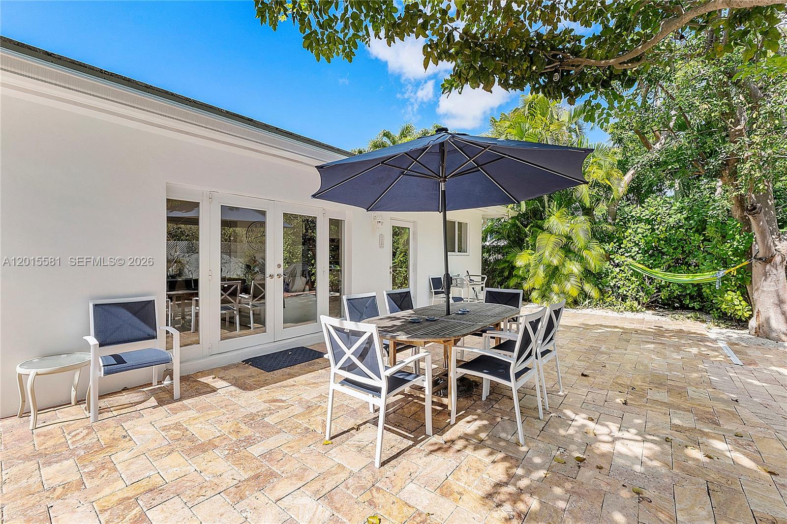 A patio with a dining set and umbrella sits outside a white house with doors — 301 Hampton Ln, Key Biscayne FL 33149, KEY BISCAYNE, FL
