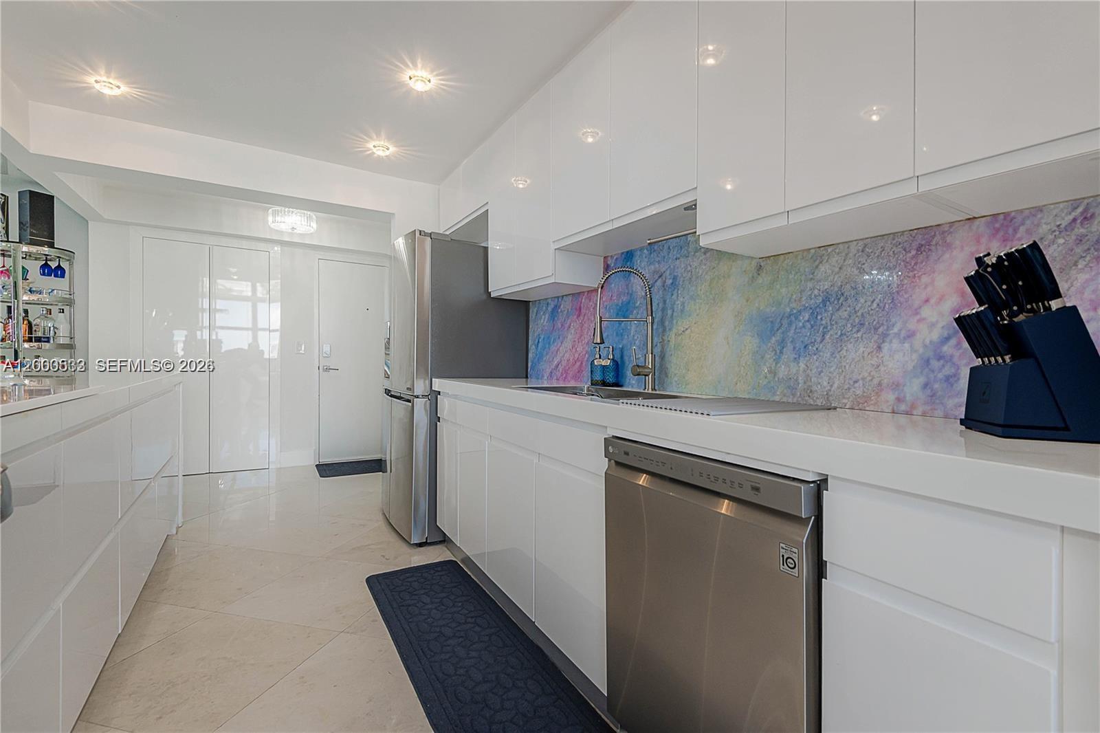 A modern kitchen features white glossy cabinets, stainless steel appliances, and a colorful patterned backsplash — 2301 S Ocean Dr # 2003, Hollywood FL 33019, HOLLYWOOD, FL
