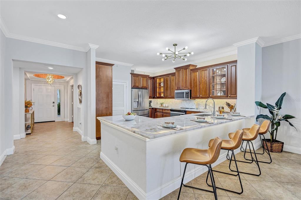 A kitchen features a marble-topped island with bar stools, wooden cabinetry, and tile flooring — 2925 TERRA CEIA BAY BOULEVARD UNIT 2802, PALMETTO, FL