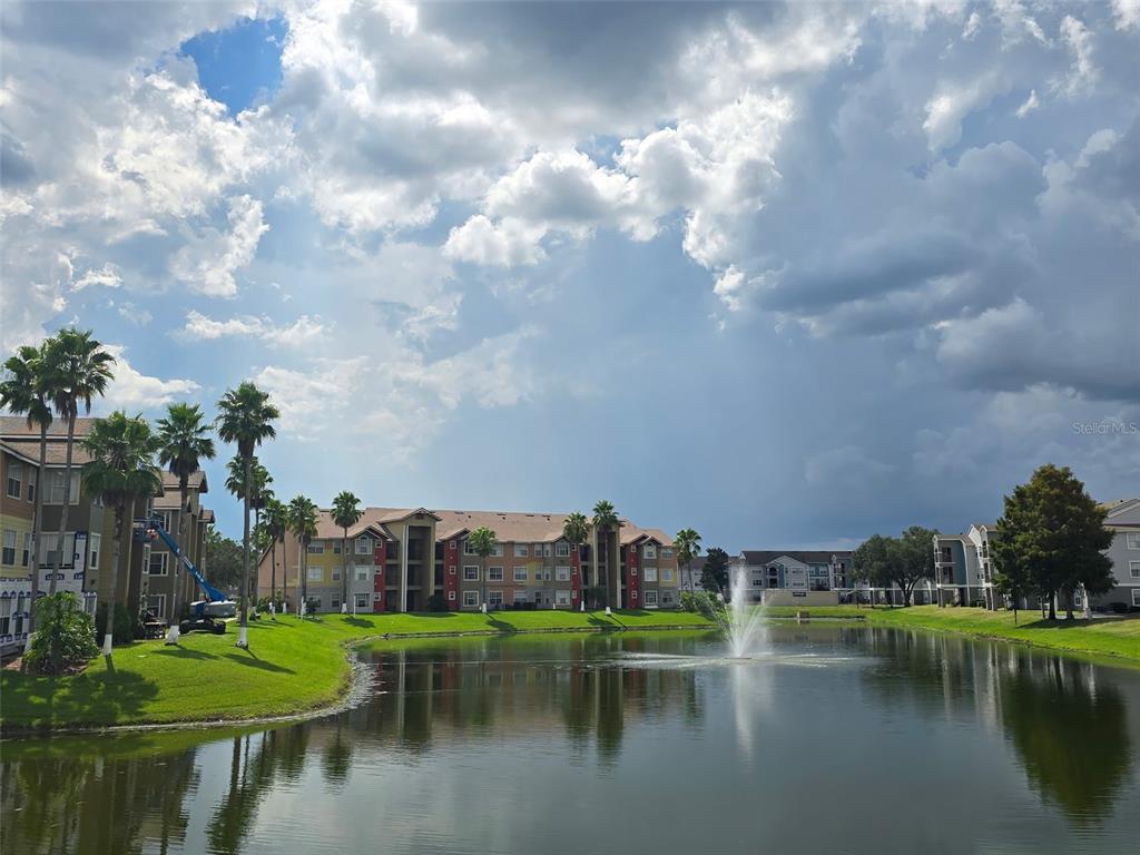 A multi-story apartment complex sits behind a pond with a fountain and palm trees — 2206 ANTIGUA PLACE, KISSIMMEE, FL