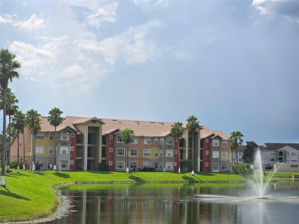 A multi-story apartment building stands behind a pond with a fountain and palm trees — 2206 ANTIGUA PLACE, KISSIMMEE, FL
