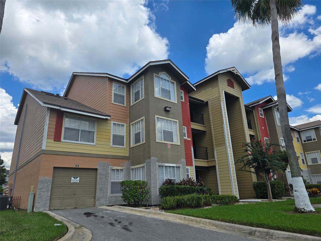 A multi-story apartment building with a garage, colorful siding, and a palm tree in front — 2206 ANTIGUA PLACE, KISSIMMEE, FL