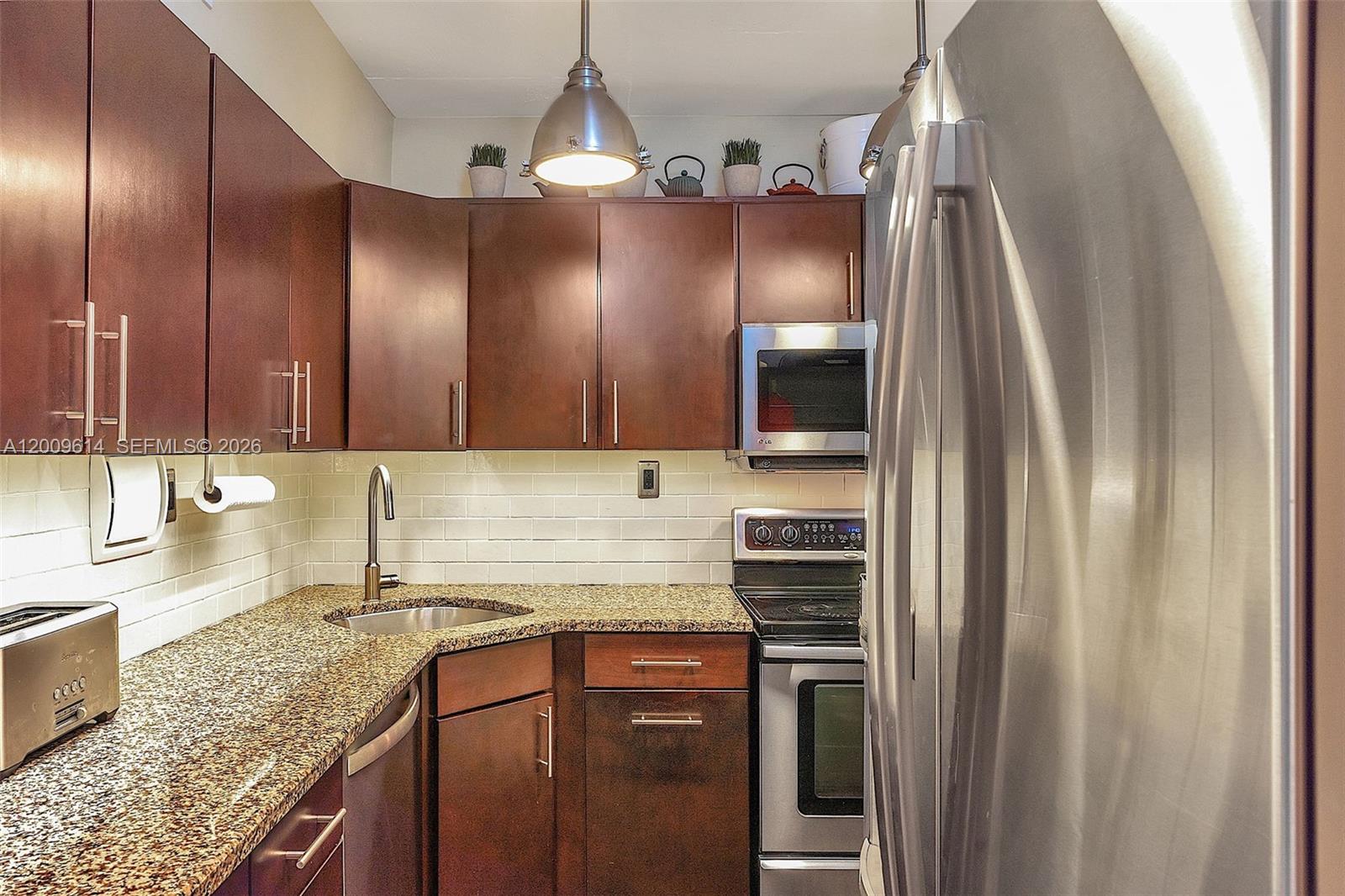A compact kitchen features dark wood cabinets, granite countertops, stainless steel appliances, and subway tile — 1200 West Ave # 423, Miami Beach FL 33139, MIAMI BEACH, FL