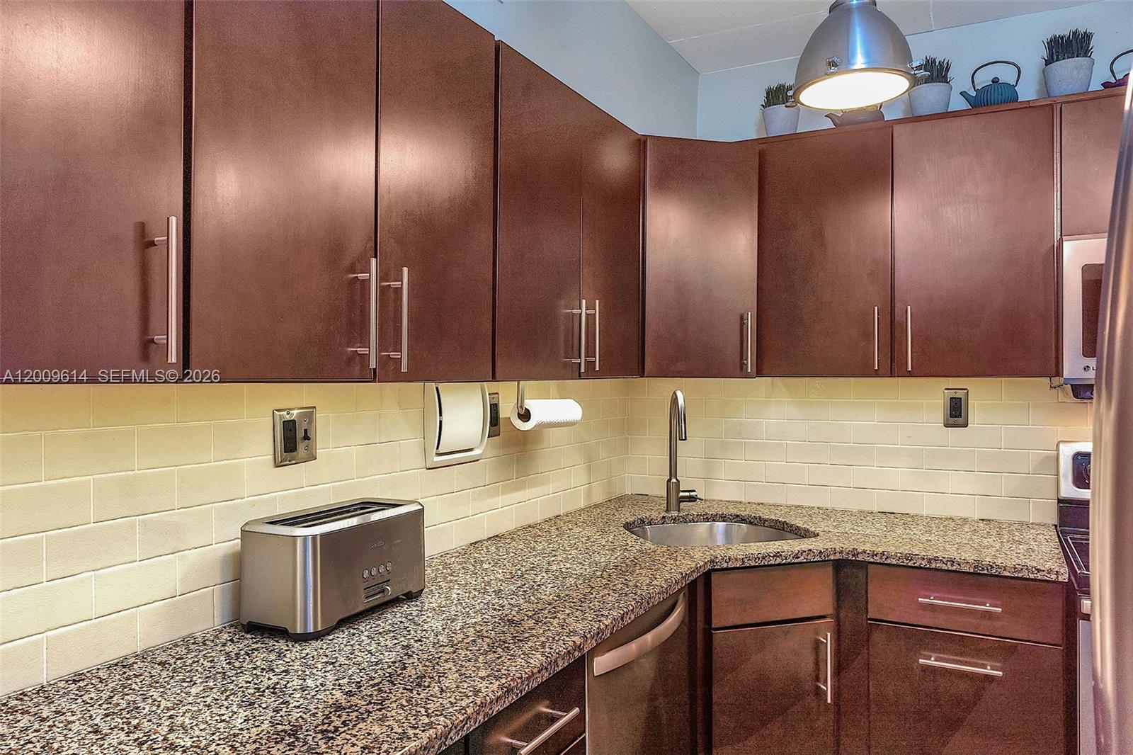 A kitchen features dark brown cabinets, granite countertops, a stainless steel sink, and subway tile — 1200 West Ave # 423, Miami Beach FL 33139, MIAMI BEACH, FL