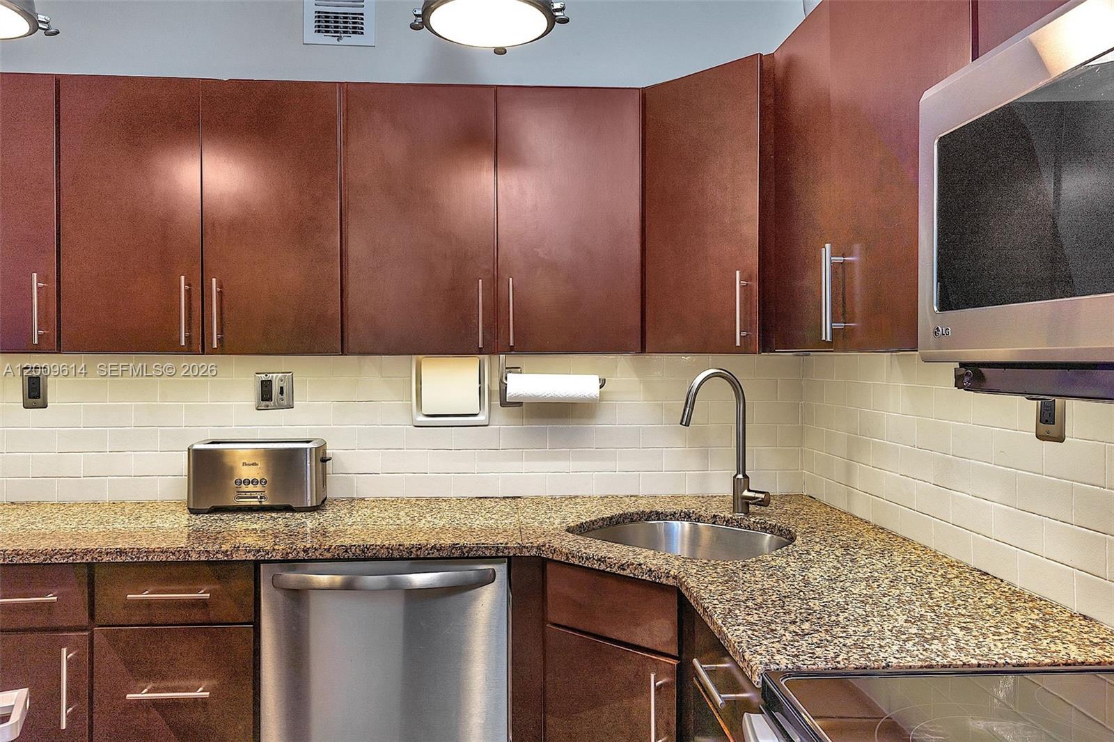 A kitchen features brown cabinets, granite countertops, a stainless steel sink, and a subway tile backsplash — 1200 West Ave # 423, Miami Beach FL 33139, MIAMI BEACH, FL