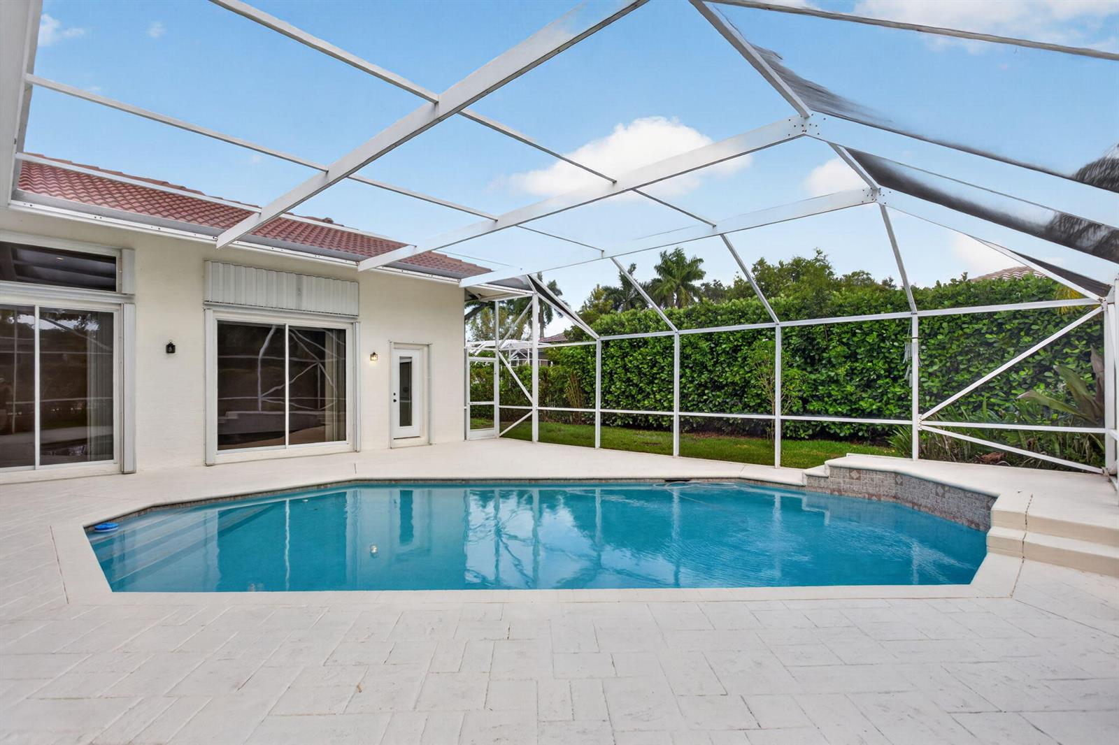 A bright living room features a beige sofa, round wooden coffee table, and sliding glass doors — 10251 NW 62nd Drive, Parkland FL 33076, PARKLAND, FL